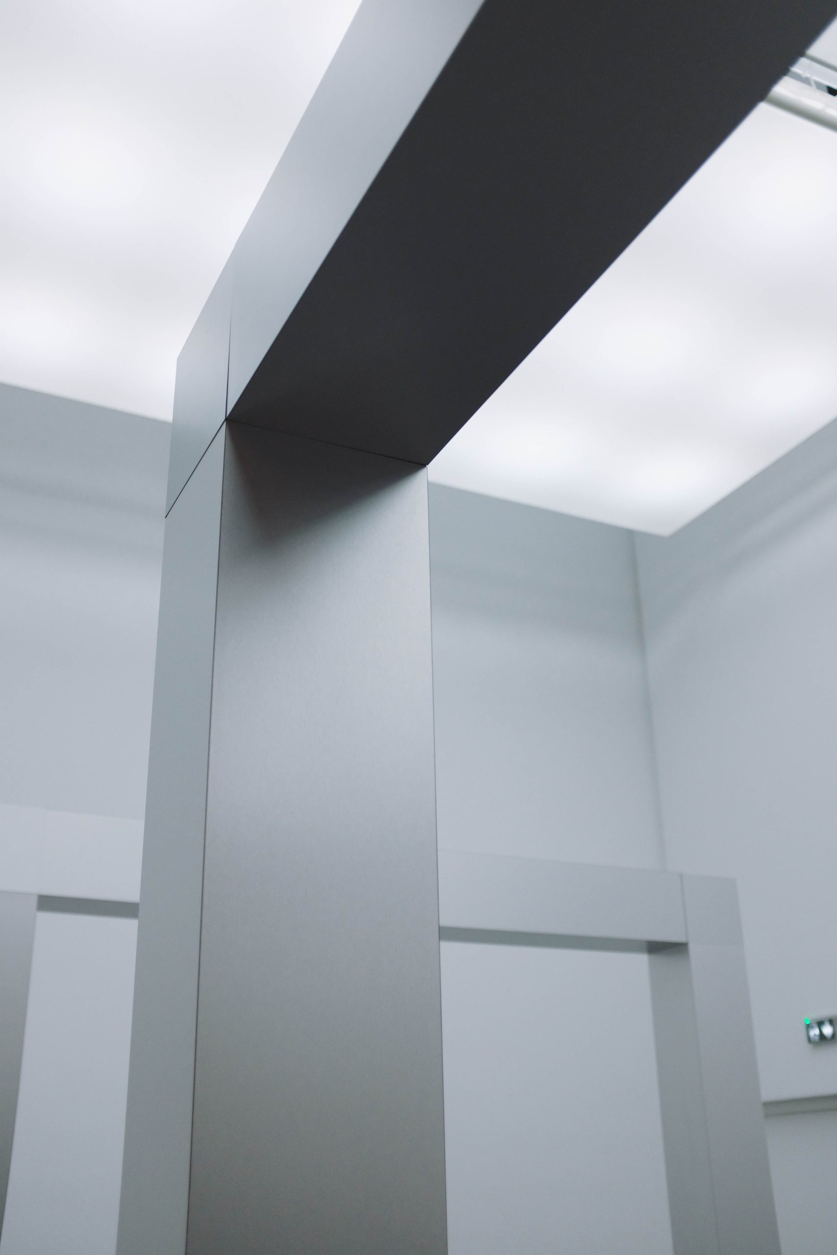 A low angle view of a corner of a silver ceiling under white lamp lights surrounded by grey walls